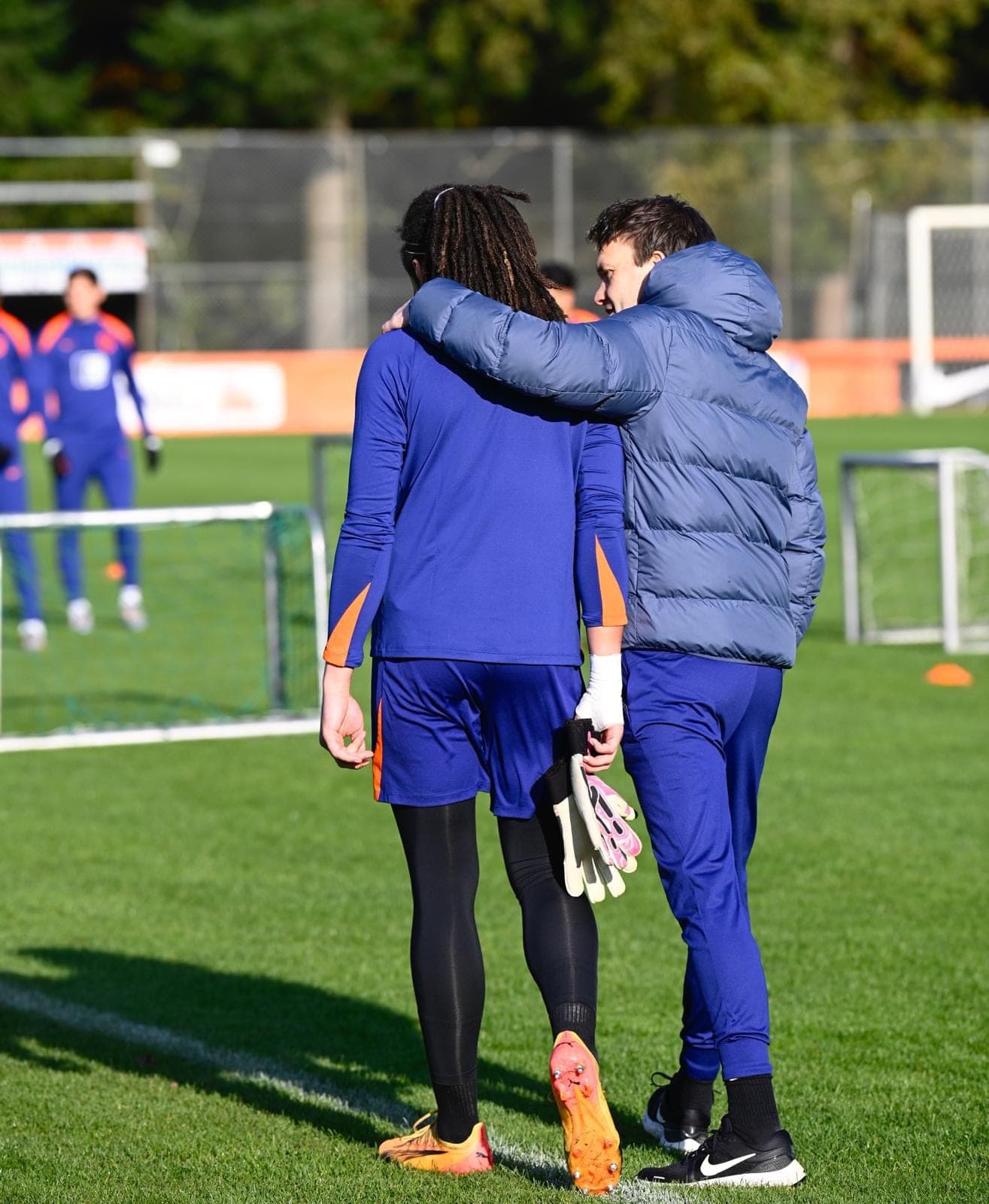 Begeleider met een arm om de schouder van een jonge keeper op het trainingsveld